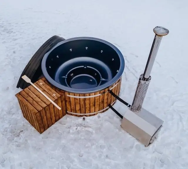 Jacuzzi extérieur en bois avec un poêle intégré, installé sur un sol enneigé, idéal pour une détente hivernale. Ce spa chauffé offre une expérience de relaxation unique, même par temps froid.