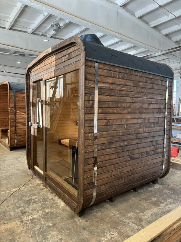 Vue d’angle d’un sauna cube 2 m en ThermoWood brun, avec porte vitrée dévoilant les banquettes intérieures