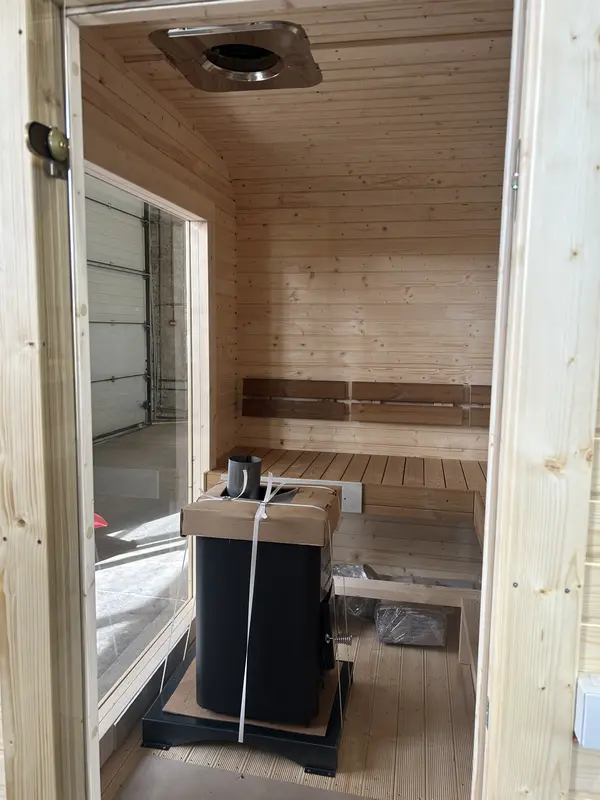 Intérieur d’un sauna cube 2 m montrant le poêle et les banquettes disposées en vis-à-vis.