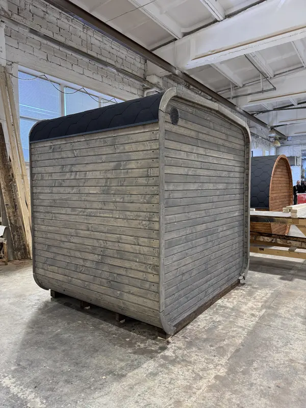 Vue latérale d’un sauna cube 2 m gris clair, sans fenêtres apparentes, posé en atelier