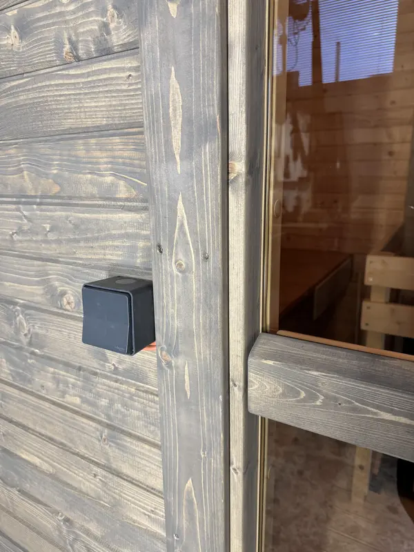 Détail extérieur d’un sauna cube en bois Thermo, gros plan sur la boîte à interrupteur posée à côté de la porte