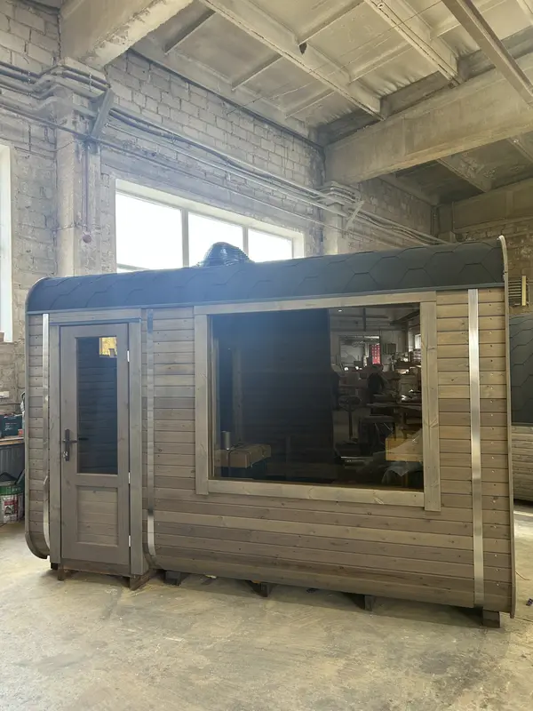 Angle avant gauche d’un sauna cube 3 m Relax en ThermoWood brun, porte vitrée et fenêtre latérale.