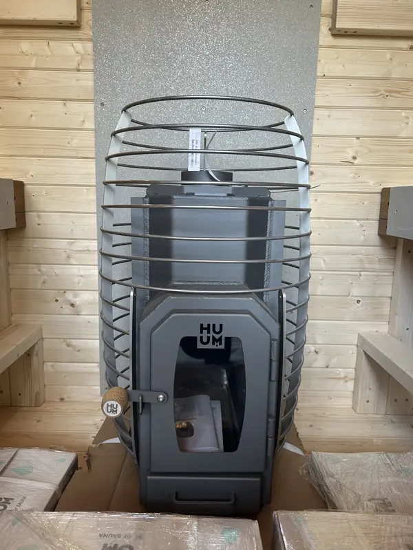 Gros plan sur un poêle HUUM en intérieur de sauna, grille de protection métallique autour de la pierre