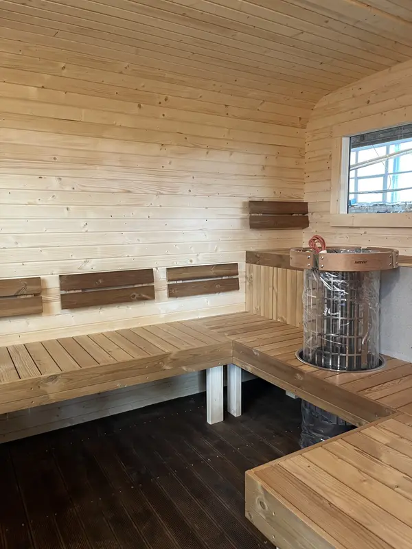 Intérieur d’un sauna cube 3 m Relax en bois clair, deux niveaux de banquettes et poêle visible dans l’angle.