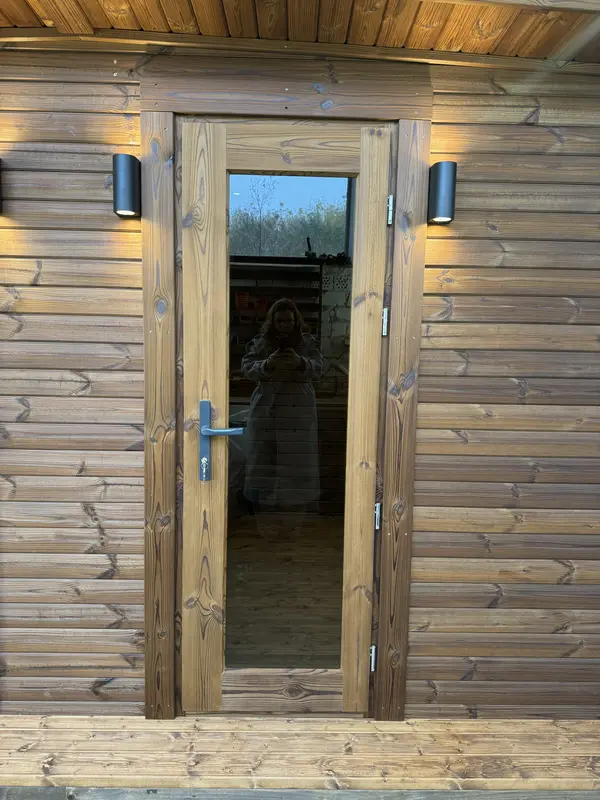 Gros plan sur la porte vitrée d’un sauna 4 m, cadre en bois naturel et poignées métalliques.