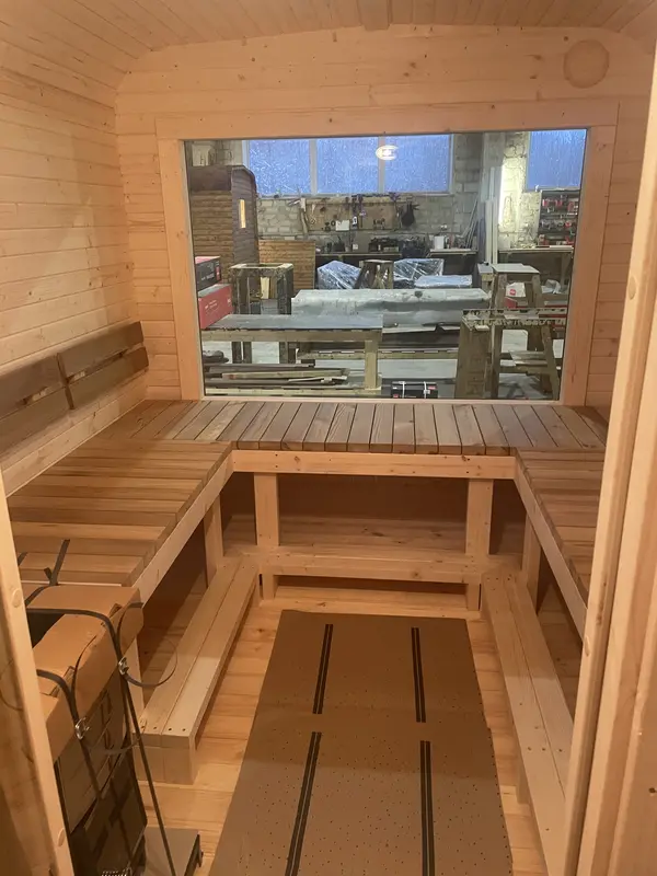 Intérieur d’un sauna cube 4 m montrant des banquettes en bois clair disposées en U autour du poêle