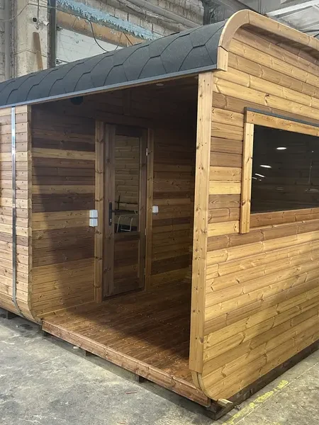Vue latérale d’un sauna cube 4 m ThermoWood brun, porte vitrée et toit cintré.