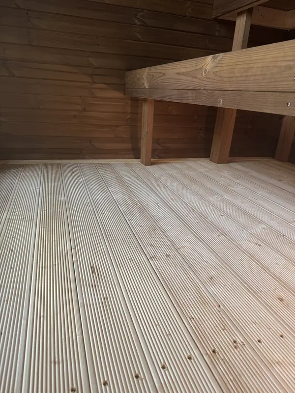 Plancher extérieur en lames de bois, détail du seuil d’un sauna 4 m de large.