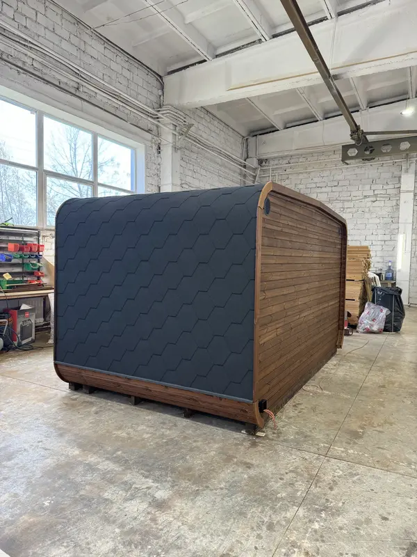 Vue arrière d’un sauna 4 m de large, toit cintré en tuiles noires et bardage ThermoWood.