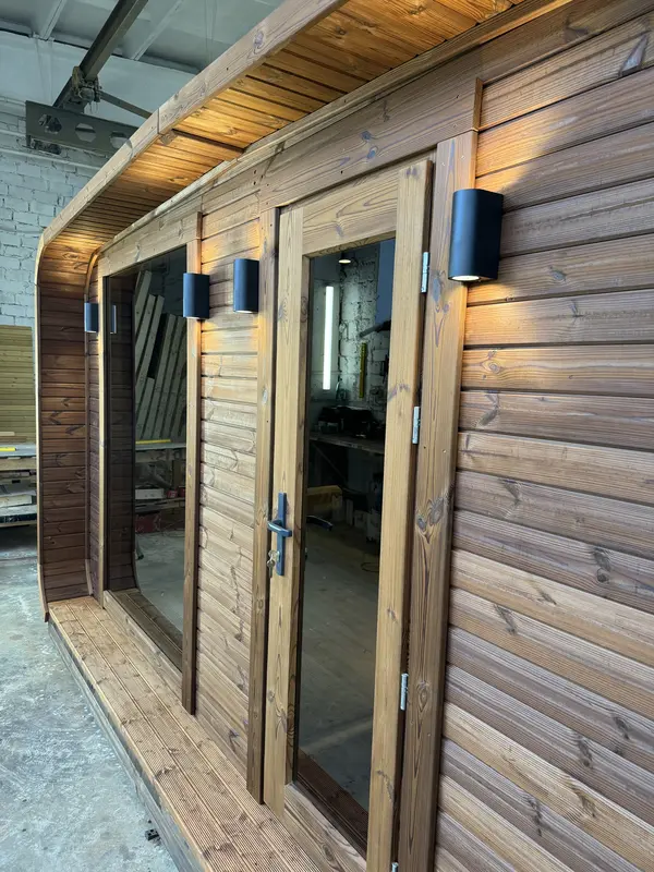 Angle d’entrée d’un sauna 4 m large, double porte vitrée sous un porche lambrissé.