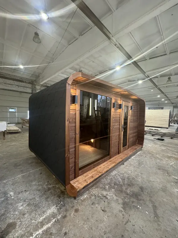 Vue d’angle d’un sauna 4 m large en ThermoWood brun foncé, porte vitrée et bardage noir mat à motifs écaillés.
