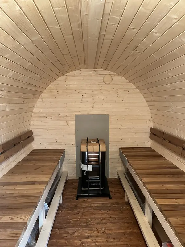 Intérieur voûté du sauna tonneau 4 m, banquettes en bois naturel et poêle Harvia visible
