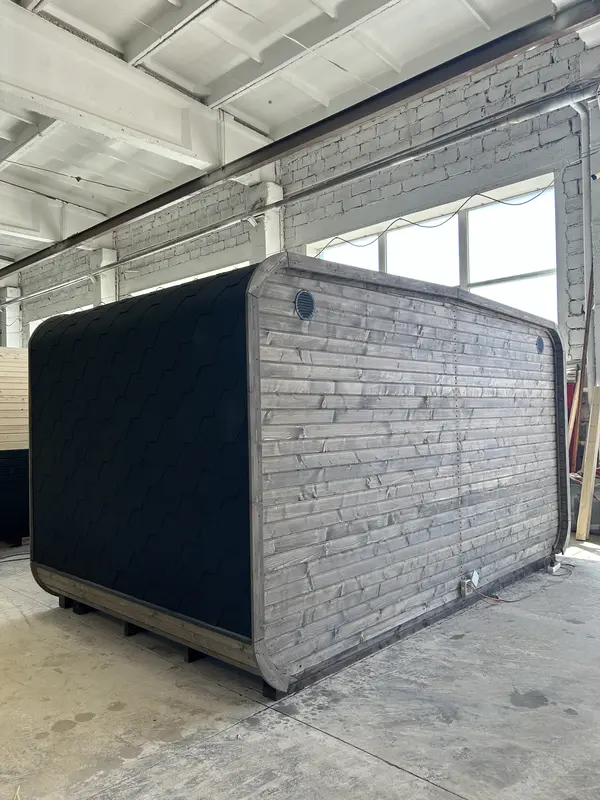 Vue arrière d’un sauna 4 m large peint en gris foncé, bardage horizontal et orifice de ventilation rond