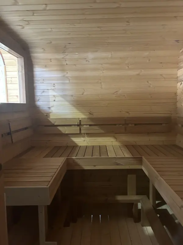Intérieur d’un sauna 4 m large, deux niveaux de banquettes en bois clair avec sol lambrissé.
