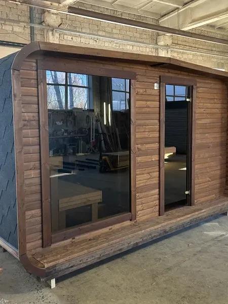 Façade d’un sauna 4 m large ThermoWood brun, double porte-vitrée et éclairage LED sous le toit.