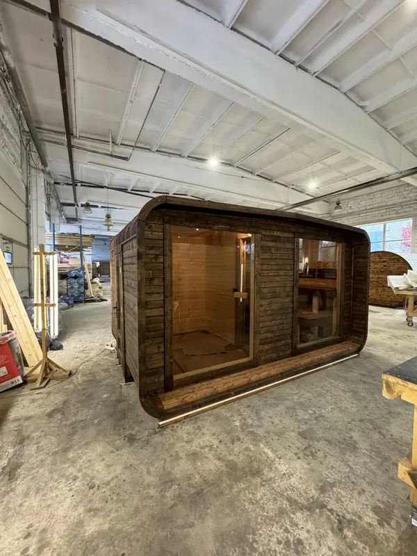 Profil latéral d’un sauna 4 m large, large baie vitrée panoramique et toiture cintrée en tôle noire.