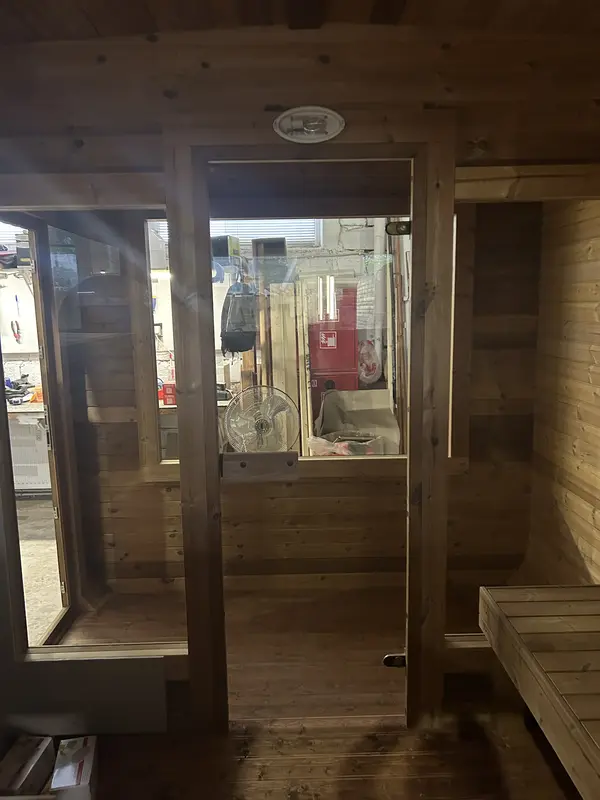 Façade avant d’un sauna cube 4 m en bois naturel, double porte vitrée laissant entrevoir l’intérieur