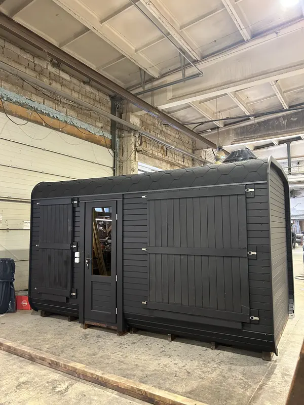 Deux modules sauna cube 4 m noirs côte à côte, portes vitrées et toit arrondi, en atelier.