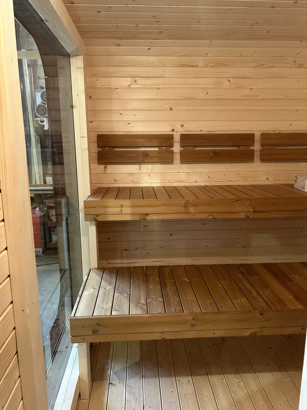 ntérieur du sauna 4 m large montrant deux niveaux de banquettes en bois lambrissé clair et mur lambrissé.