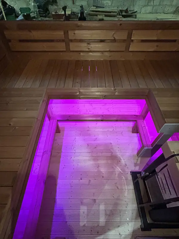Banquettes intérieures d’un sauna cube 4 m éclairées par des LED sous les lattes, lumière violette.