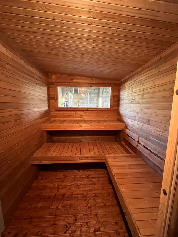 Gros plan intérieur de sauna en bois foncé avec trois niveaux de banquettes contre un mur lambrissé.
