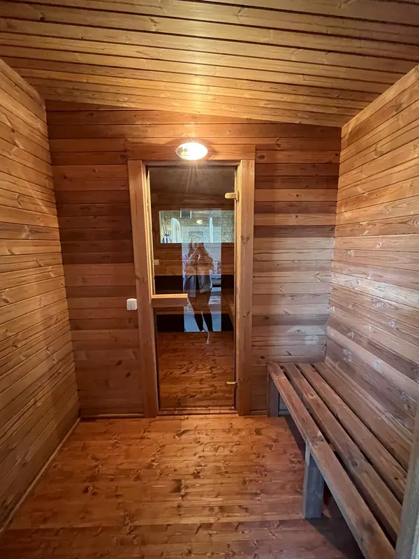 Entrée intérieure d’un sauna lambrissé, porte vitrée droite et banc fixe sur le côté.