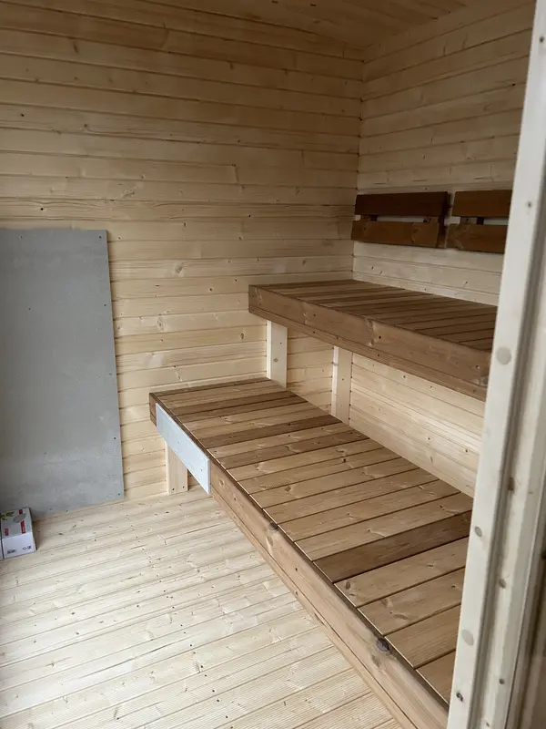 Intérieur de sauna box clair avec deux niveaux de bancs en bois et sol lambrissé.