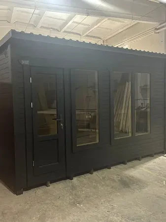 Sauna modulable peint en noir avec double porte vitrée et toit en tôle ondulée, en atelier.