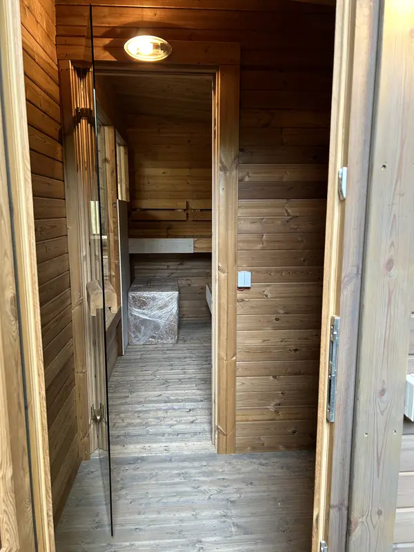 Couloir d’entrée intérieur d’un sauna box 4 m, mur lambrissé clair et seuil de la porte vitrée.