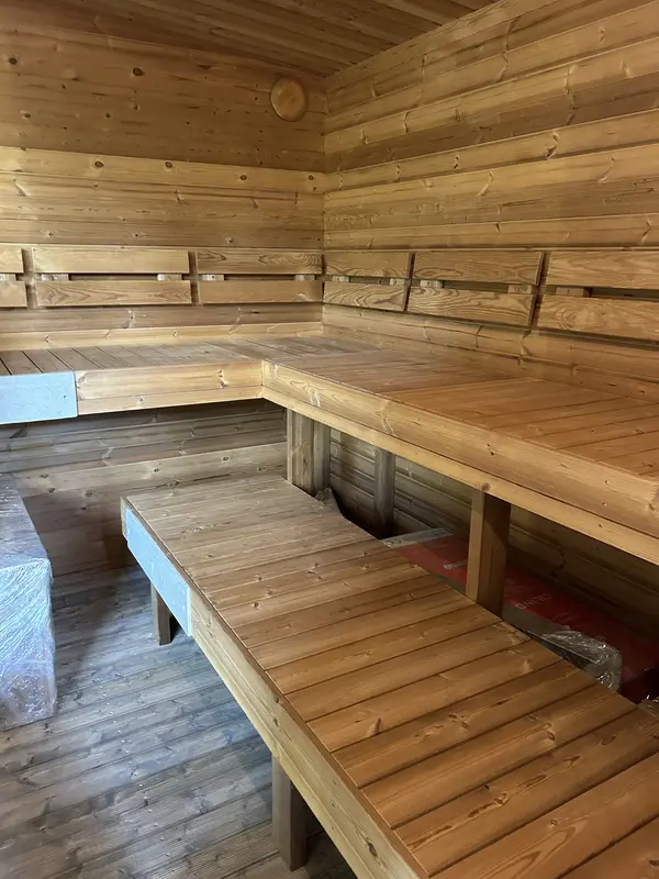 Intérieur d’un sauna box 4 m montrant deux niveaux de bancs en bois clair formant un L, parois lambrissées.