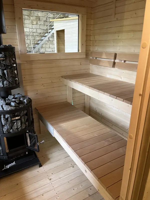 Détail intérieur d’un sauna box 4 m sur deux niveaux de bancs en bois naturel sous une fenêtre.