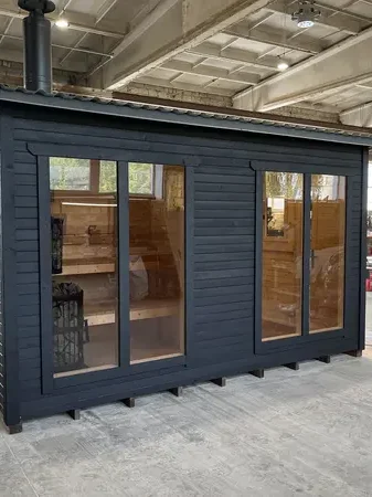 Façade d’angle d’un sauna box 4 m peint en noir, double porte vitrée et grande fenêtre latérale, en atelier.