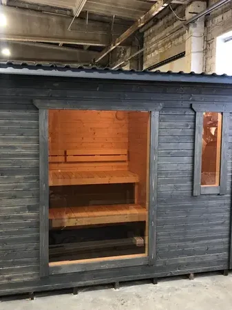 Sauna box peint en noir, vue frontale avec porte vitrée gauche ouverte et banquettes intérieures visibles.