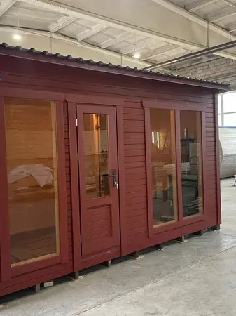 Sauna modulable peint en rouge brique avec deux fenêtres vitrées et porte vitrée, en atelier.