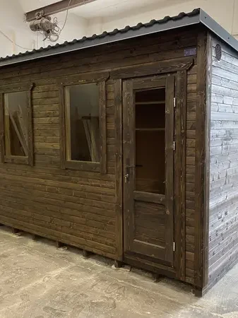Sauna modulable ThermoWood foncé en atelier, vue d’angle montrant trois fenêtres latérales et porte vitrée.