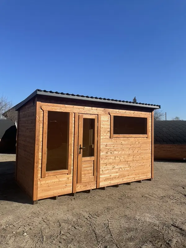 Sauna box ThermoWood brut posé en extérieur sous un ciel bleu, double porte vitrée et petite fenêtre latérale.