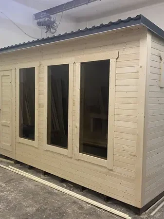 Sauna box lambrissé clair avec trois fenêtres verticales alignées sur la façade, en hangar.
