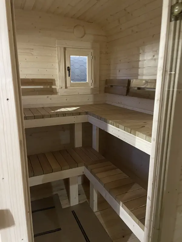 Intérieur d’un sauna cube 5 m Relax, deux niveaux de bancs en bois naturel formant un angle droit.