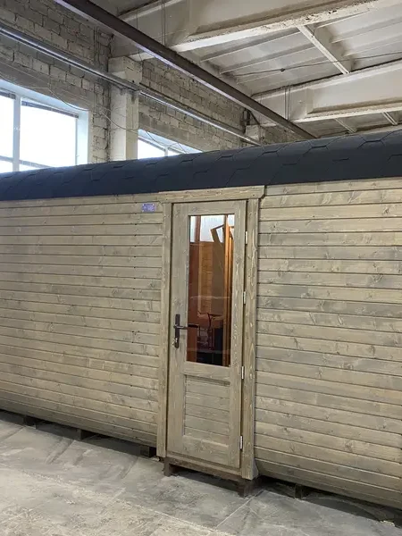 Vue latérale d’un sauna cube 5 m Relax gris clair, porte vitrée et fenêtre panoramique.