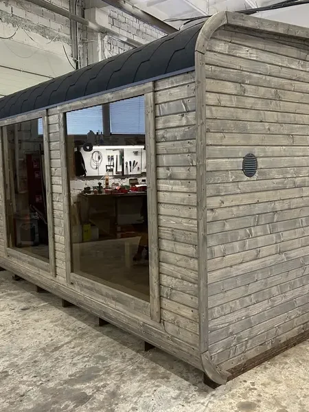 Vue d’angle extérieur d’un sauna cube 5 m peint en gris clair, porte-vitrée et toit arrondi.