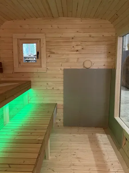 Banquettes intérieures d’un sauna cube 5 m, éclairage LED vert sous les lattes en bois clair.