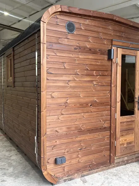 Angle arrière d’un sauna cube 5 m ThermoWood brun, parois lambrissées et orifice de ventilation circulaire.