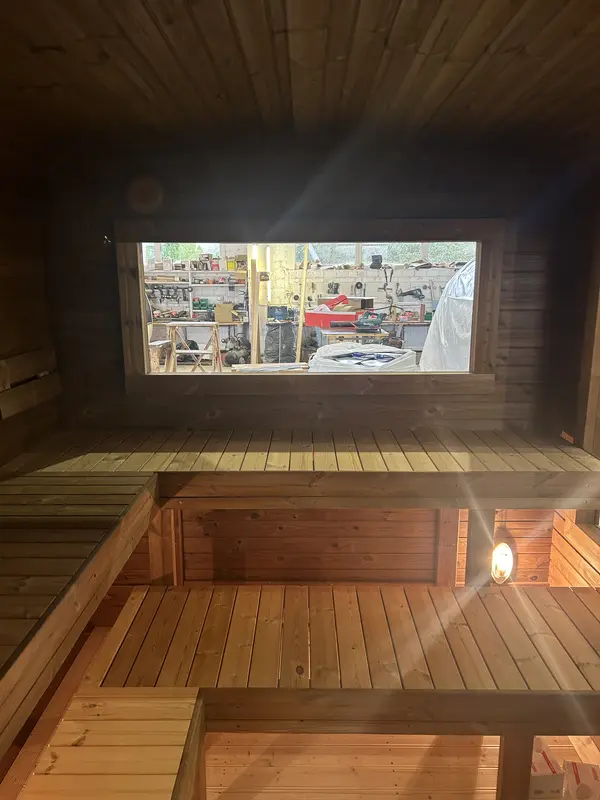 Banquettes en U d’un sauna cube 5 m, éclairage naturel par fenêtre panoramique frontale.