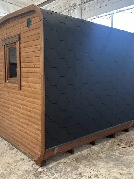 Vue arrière d’un sauna cube 5 m avec toit arrondi recouvert d’écailles noires et bardage brun.
