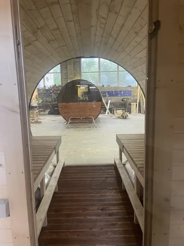 **Vue depuis l’intérieur du sauna tonneau 5 m Relax, regardant vers un autre sauna en arrière-plan**
