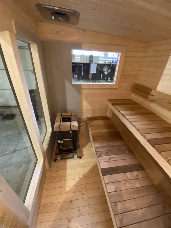 Détail intérieur d’un sauna box 5 m, banquettes en bois clair à deux niveaux et sol lambrissé.
