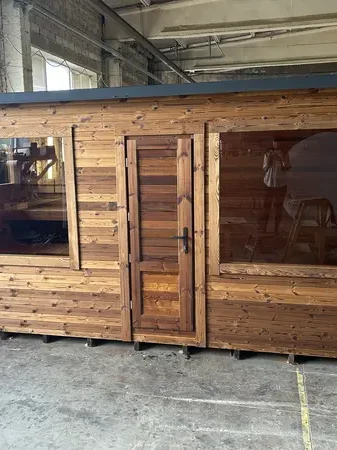 Vue frontale d’un sauna modulable 5 m en ThermoWood naturel, deux larges baies vitrées et porte vitrée, en atelier.