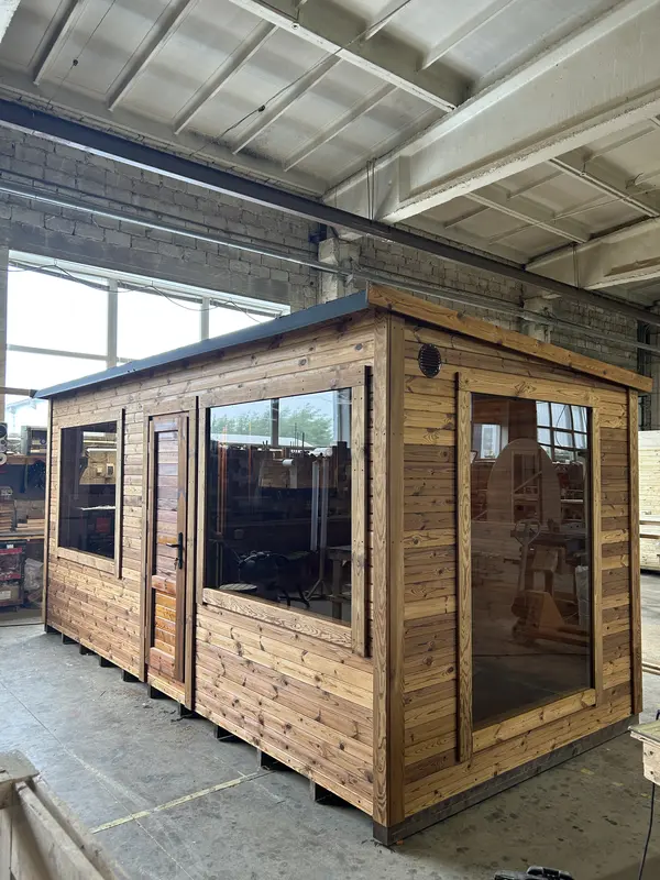 Angle avant d’un sauna modulable 5 m en ThermoWood naturel, avec grandes baies vitrées sur deux façades, en atelier.