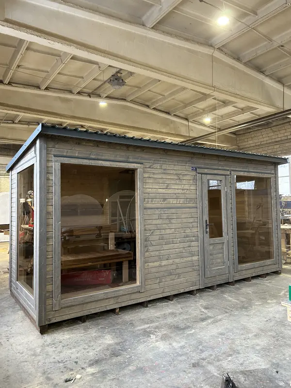 Vue avant d’un sauna box 5 m gris, double porte vitrée et fenêtre hauteur sous un toit plat, en atelier.