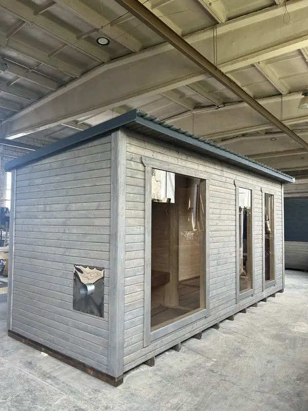 Vue latérale d’un sauna modulable 5 m peint en gris clair, avec deux larges fenêtres panoramiques, en hangar.